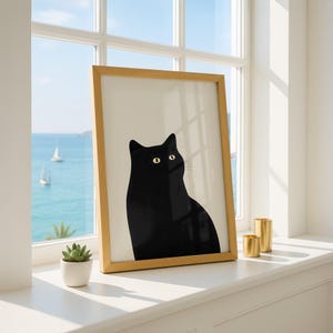 Könnte beinhalten: Ein gerahmter Kunstdruck mit einer minimalistischen Illustration einer einfarbigen schwarzen Katze mit großen, blassgelben Augen vor einem cremeweißen Hintergrund. Das Kunstwerk befindet sich in einem hellen Holzrahmen und wirkt schlicht.