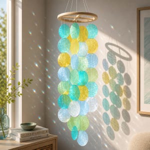 May include: A decorative wind chime featuring a wooden ring and strings of translucent, circular discs in shades of blue, green, and yellow. The chime hangs in front of a window, with sunlight creating patterns on the wall.