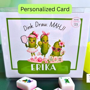 May include: A rectangular personalized card in a clear plastic sleeve featuring the text Dink. Draw. MAHJ! and the name ERIKA. The illustration shows three green pickle characters playing pickleball and mahjong with paddles and tiles.