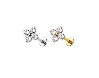 May include: Two lip piercing studs. One is silver-toned, the other gold-toned. Each features a four-petal flower design with clear, round gemstones. The studs are set against a white background.