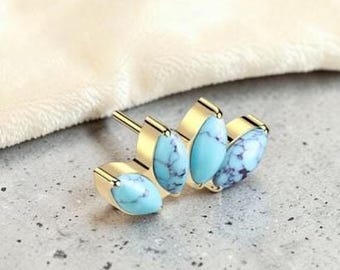 May include: Gold-toned stud earrings featuring oval turquoise stones with dark blue veining. The earrings have a post back and are set against a neutral background. The earrings are a jewelry item.