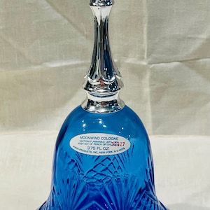 May include: A cobalt blue glass bell-shaped cologne bottle with a silver-colored metal top and stem. The bottle has a textured pattern and a label that reads "MOONWIND COLOGNE". The bottle is 3.75 fl oz.