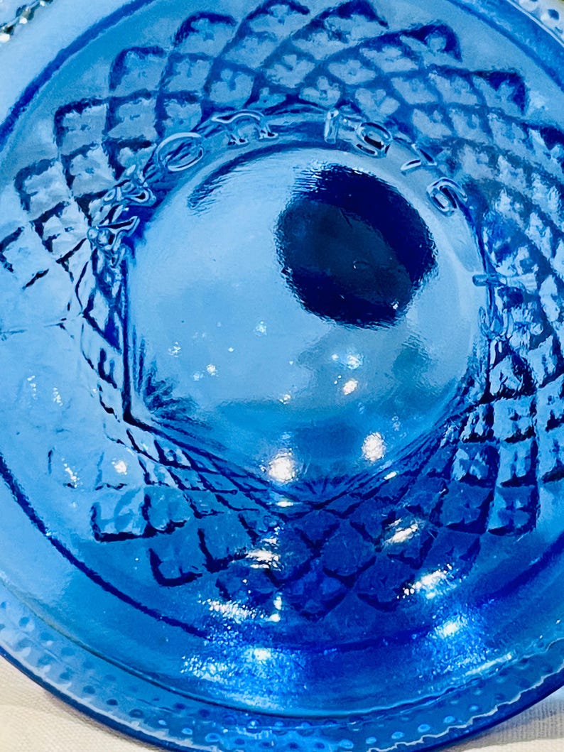 May include: Close-up of a vibrant blue glass object with a diamond pattern. The object has a circular shape with a textured surface and a central indentation. The glass reflects light, creating highlights and shadows.