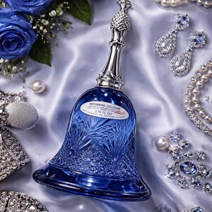 May include: A cobalt blue bell-shaped cologne bottle with a silver handle and a pineapple-shaped stopper. The bottle is surrounded by blue roses, jewelry, and pearls. The label reads "Moonwind Cologne 3.75 FL OZ".