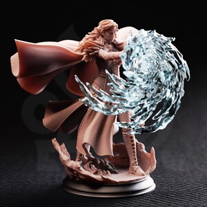 Könnte beinhalten: Detaillierte Figur einer weiblichen Fantasy-Figur mit langen blonden Haaren, die einen fließenden Umhang und eine Rüstung trägt. Sie wird dargestellt, wie sie eine wirbelnde, durchscheinende blaue Energieexplosion beschwört. Der Sockel ist strukturiert und hellbraun.