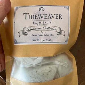 May include: A tan paper pouch containing three white sachets of Tideweaver bath salts from the Lunaria Collection by Llama Farm Labs, LLC. The label features the text Net Wt. 12 oz / 340 g and a Cancer zodiac symbol at the top of the packaging.