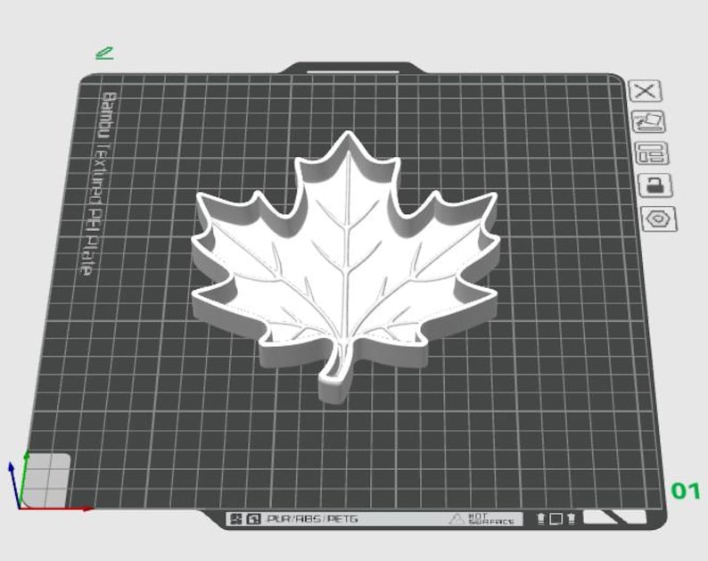 Puede incluir: Un cortador de galletas con forma de hoja de arce impreso en 3D en color blanco, centrado sobre una placa de construcci&oacute;n gris oscuro con patr&oacute;n de rejilla. La placa muestra el texto Bambu Textured PEI Plate y etiquetas de material.