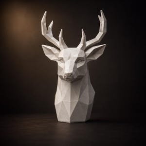 May include: A white deer head sculpture featuring a geometric, faceted design. The bust displays sharp, angular planes forming the face, ears, and large antlers, creating a structured, multi-faceted appearance with a smooth, matte finish.