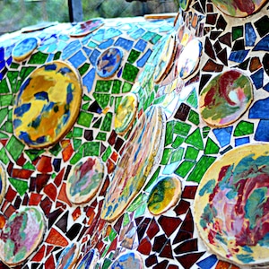 May include: A colorful mosaic wall art piece made of broken tiles in various shades of blue, green, red, yellow, and white. The tiles are arranged in a random pattern, creating a visually appealing and abstract design.