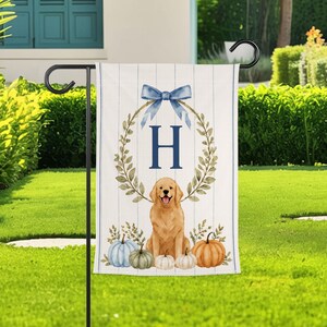 Peut inclure: Un drapeau de jardin vertical avec un fond blanc à fines rayures bleues. Le motif comprend un nœud bleu en haut, une lettre H centrale, un chien golden retriever et une collection de citrouilles dans des tons de bleu, vert et orange.