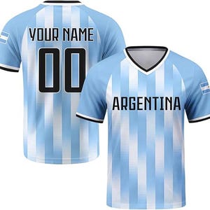 May include: A light blue and white vertical striped jersey with a V-neck collar. The front features the text ARGENTINA in black, while the back displays the text YOUR NAME and the number 00 in black. Both sleeves feature a small Argentina flag patch.