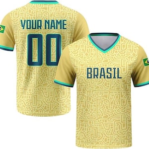 May include: A yellow V-neck jersey featuring a complex maze-like pattern in a lighter shade. The front displays the text BRASIL in dark blue, while the back shows YOUR NAME and the number 00. Both sleeves feature a small Brazil flag patch.