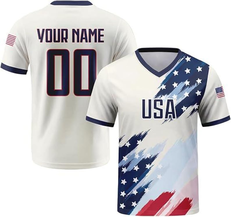 May include: A short-sleeved V-neck jersey featuring a cream base with a blue and red brushstroke flag pattern, the text USA, and a small flag on the sleeve. The back displays the text YOUR NAME and the number 00 in dark blue with red outlines.