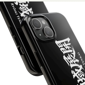 Peut inclure: Coque de téléphone noire avec texte japonais blanc. La coque a une finition brillante et un cadre de caméra surélevé. Le texte comprend les mots "Ryoki Tenkai". La coque est conçue pour protéger l'appareil photo et le corps du téléphone.