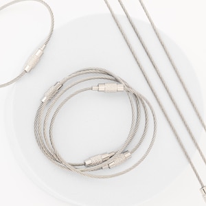 May include: Five silver metal keychains with a braided cable design and silver metal clasps. The keychains are arranged in a circle on a white surface.