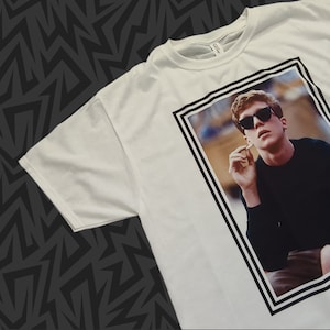 Könnte beinhalten: Weißes T-Shirt mit einem schwarz-weiß gerahmten Bild einer Person mit Sonnenbrille und schwarzem Hemd. Die Person hält eine Zigarette in der Hand.