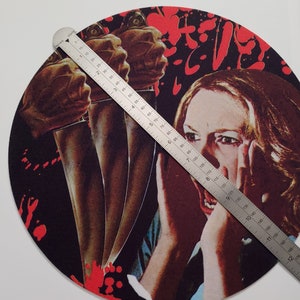 May include: A round black and red mousepad with a graphic of a woman screaming with three knives behind her. The woman is wearing a blue and white shirt. The mousepad is 9 inches in diameter.