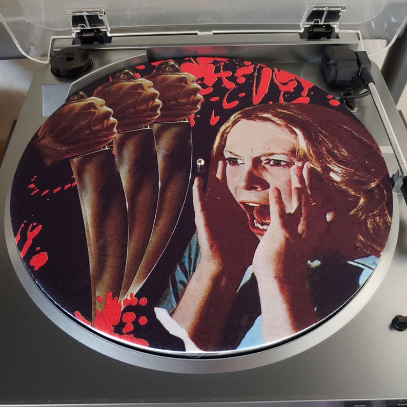 May include: A black and red vinyl record slipmat featuring a woman with her hands over her face screaming, with three knives in the background.