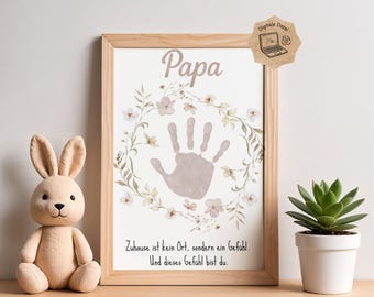 May include: A framed print with the word "Papa" and a handprint in the center, surrounded by a floral wreath. The print also includes German text. A plush bunny and a potted succulent sit nearby.