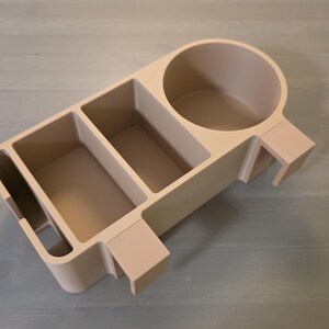 May include: A beige plastic desk organizer featuring a circular cup holder on one side, two rectangular storage compartments in the center, and a narrow vertical slot on the opposite end, all integrated into a single, unified structure.