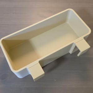 May include: A rectangular, off-white plastic storage bin featuring a hollow interior and two integrated hooks on one side, designed for hanging or mounting. The container has smooth, rounded corners and a solid, uniform matte finish throughout.
