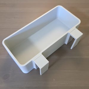May include: A rectangular white plastic storage bin featuring an open top and two integrated hooks on one side, designed to hang over the edge of a flat surface. The container has smooth, rounded corners and a clean, solid white finish throughout.