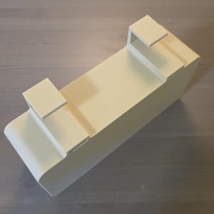 May include: A rectangular, off-white metal storage bin featuring two integrated hooks on the top edge. The container has a smooth, solid finish with rounded corners on one side and a flat, open-top design, constructed for hanging or mounting purposes.