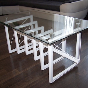 Può includere: Un tavolino rettangolare moderno con un piano in vetro trasparente e una struttura in metallo bianco. La struttura del tavolo ha un design geometrico unico. Il tavolo misura circa 122 cm di lunghezza, 61 cm di larghezza e 41 cm di altezza.