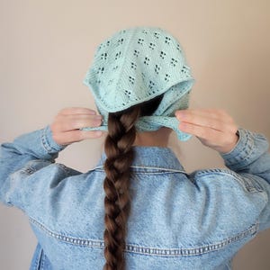 May include: A light mint green knit headscarf featuring a delicate openwork diamond pattern. The triangular fabric is tied at the back of the head with two thin knit straps, showcasing a textured, breathable design made from soft yarn.