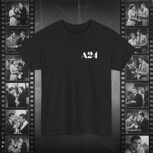 Puede incluir: Una camiseta negra de manga corta con el texto blanco A24 impreso en la parte superior del pecho. La prenda tiene cuello redondo y un corte estándar, presentada sobre un fondo de tiras de película verticales con fotos en blanco y negro.