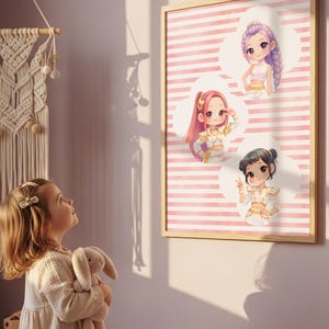 Op de afbeelding: Een ingelijste kunstprint met drie chibi-stijl figuren in wit met gouden outfits tegen een achtergrond van horizontale roze en witte strepen. De figuren zijn gerangschikt in witte wolkachtige vormen en hebben elk een ander kapsel.