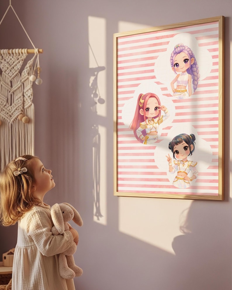 Op de afbeelding: Een ingelijste kunstprint met drie chibi-stijl figuren in wit met gouden outfits tegen een achtergrond van horizontale roze en witte strepen. De figuren zijn gerangschikt in witte wolkachtige vormen en hebben elk een ander kapsel.