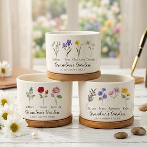 Puede incluir: Tres macetas de cerámica blanca con diseños florales y platillos de madera. Cada maceta está personalizada con nombres y el texto "Grandma's Garden LOVE GROWS HERE". Las macetas están apiladas sobre una superficie de madera blanca.