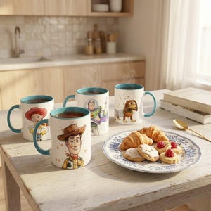 May include: Four white ceramic mugs with teal rims and handles, each featuring a different character illustration from the Toy Story franchise, including Woody, Jessie, Buzz Lightyear, and Slinky Dog, arranged on a wooden table with a plate of pastries.