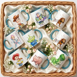 May include: A collection of nine white ceramic mugs with light blue handles, each featuring a different colorful cartoon character illustration, arranged in a wicker basket lined with cream-colored fabric and decorated with small pink roses.