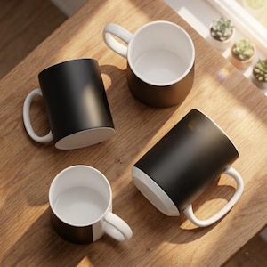 May include: Four ceramic mugs with a matte black exterior and a glossy white interior. Each mug features a white handle. Two mugs are positioned upright showing the white interior, while two mugs are lying on their sides showing the black exterior.