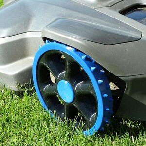 Peut inclure: Une tondeuse à gazon robotisée dotée d'un châssis en plastique gris lisse et d'une roue proéminente avec un design noir à cinq rayons, un rebord extérieur bleu vif et de petits picots bleus sur le bord pour l'adhérence, sur de l'herbe verte.