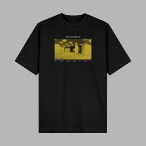 May include: A black short-sleeve t-shirt featuring a rectangular graphic print of a yellow-toned, empty office space. The text "BACKROOMS" appears above the image, with smaller white text printed below the graphic on the front of the garment.