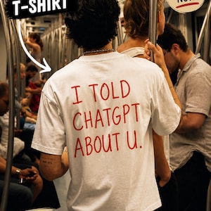 Può includere: T-shirt bianca con la scritta rossa "I TOLD CHATGPT ABOUT U." La maglietta è etichettata "VIRAL T-SHIRT" e "TRENDING NOW." L'immagine include anche il testo "PERFECT GIFT FOR FRIENDS."