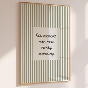May include: A framed print with a gold border. The print features a striped background in shades of green and white. A central square contains the handwritten text: "his mercies are new every morning."