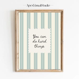 Peut inclure: Une affiche encadr&eacute;e avec un fond &agrave; rayures verticales bleu clair et cr&egrave;me. Au centre, un rectangle festonn&eacute; de couleur cr&egrave;me contient le texte gris fonc&eacute; "You can do hard things" &eacute;crit dans une police d'&eacute;criture cursive.