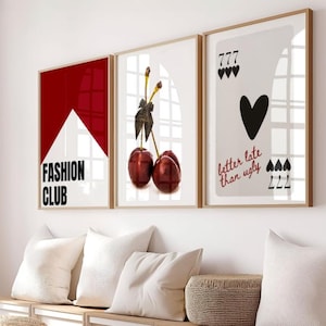 May include: Three framed art prints with a modern aesthetic. One features a red and white geometric design with "FASHION CLUB" text. Another showcases cherries, and the third displays a playing card design with the text "better late than ugly."