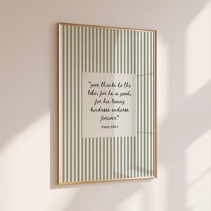 May include: A rectangular wall art print in a thin gold frame featuring a vertical sage green and white striped pattern. A central white square contains the black cursive text: "give thanks to the lord, for he is good, for his loving kindness endures forever" Psalm 136:1.