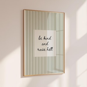 Könnte beinhalten: Ein gerahmter Druck mit goldenem Rahmen. Der Druck hat einen gestreiften Hintergrund in Grün und Weiß. Ein weißes Quadrat in der Mitte enthält den handgeschriebenen Text "be kind and raise hell" in schwarzer Schreibschrift.