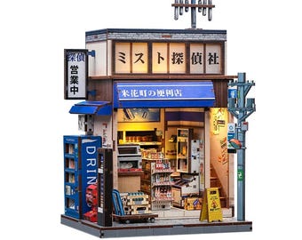 May include: A detailed miniature Japanese convenience store model. It features a blue awning, illuminated signs, and shelves stocked with miniature products. Includes Japanese text and a street scene.