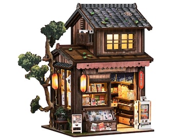 May include: A miniature Japanese shop model with a detailed wooden exterior, featuring a tiled roof, paper lanterns, and a small tree. The shop's interior is illuminated, showcasing shelves of miniature products and a vending machine.