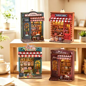 May include: Four miniature wooden shop models featuring illuminated interiors. The collection includes a green coffee shop, a red bakery shop, a teal flower shop, and a dark brown bookstore, each with striped awnings and detailed storefronts.