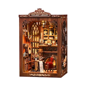 May include: A miniature wooden Twilight Library diorama with intricate details. The interior features a fireplace, bookshelves, a desk, and a red chair. The top of the diorama has the words "Twilight Library" in a decorative banner.
