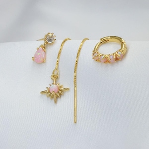 Op de afbeelding: Een collectie gouden oorbellen met roze opaal accenten. De set bevat een druppelvormige oorbel, een sterrenoorbel, een draadoorbel en een oorring met meerdere opaalstenen. De oorbellen worden gepresenteerd op een witte ondergrond.