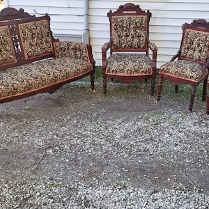 May include: A parlor furniture set consisting of one loveseat and four armchairs. Each piece features dark brown wooden frames with carved detailing and upholstered seats and backrests in a patterned fabric with gold, black, and brown floral motifs.